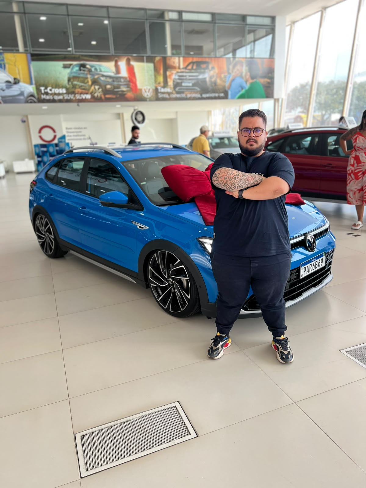 Jonathas Gomes em uma concessionária ao lado de um Volkswagen azul